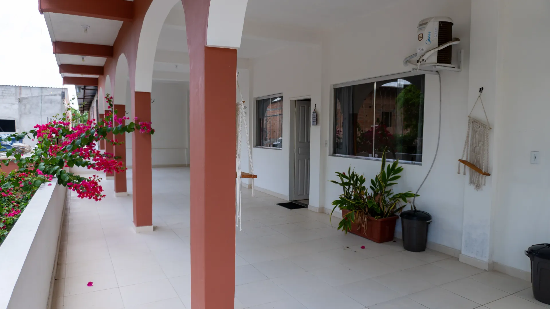 Varanda externa coberta com colunas rosas, flores e paredes brancas- Solar Café e Pousada