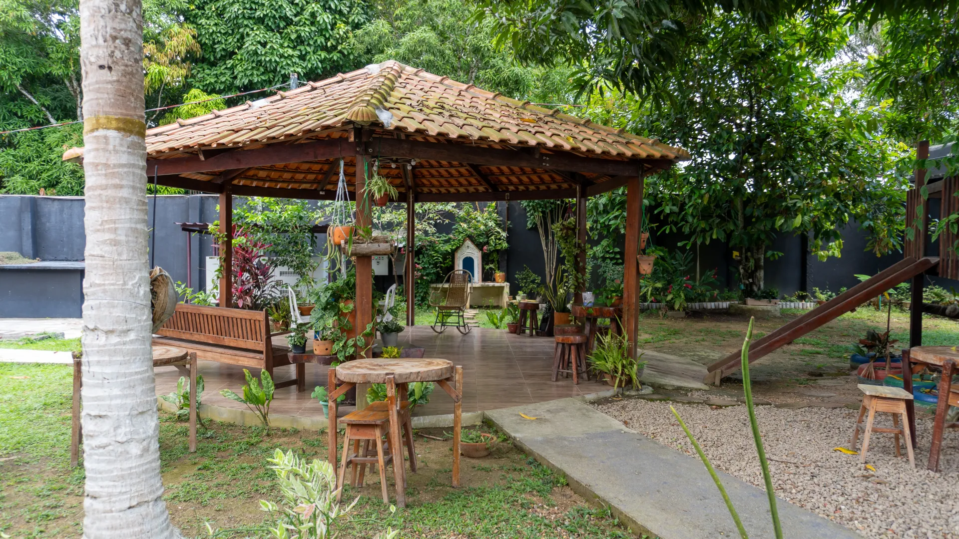 Gazebo de madeira com assentos em um jardim, cercado por árvores e uma pequena passarela - Solar Café e Pousada