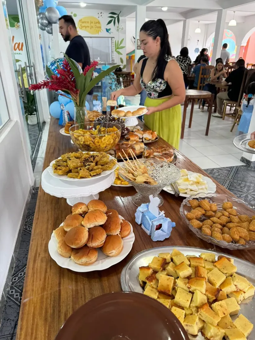 Mulher em uma mesa de bufê repleta de comida; a decoração do evento inclui balões - Solar Café e Pousada