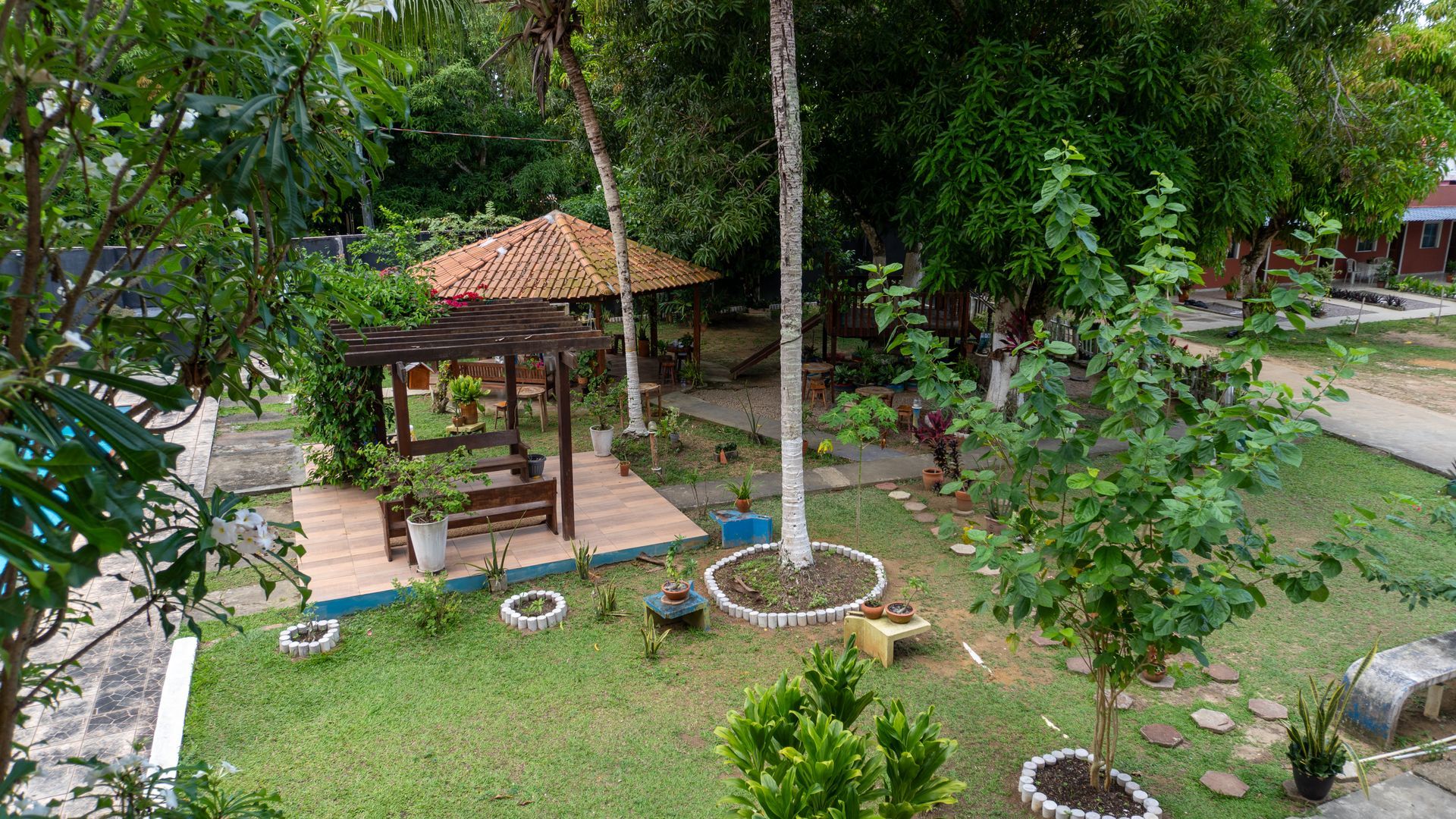 Um jardim verdejante com um gazebo, árvores e uma estrutura de telhado de telhas - Solar Café e Pousada