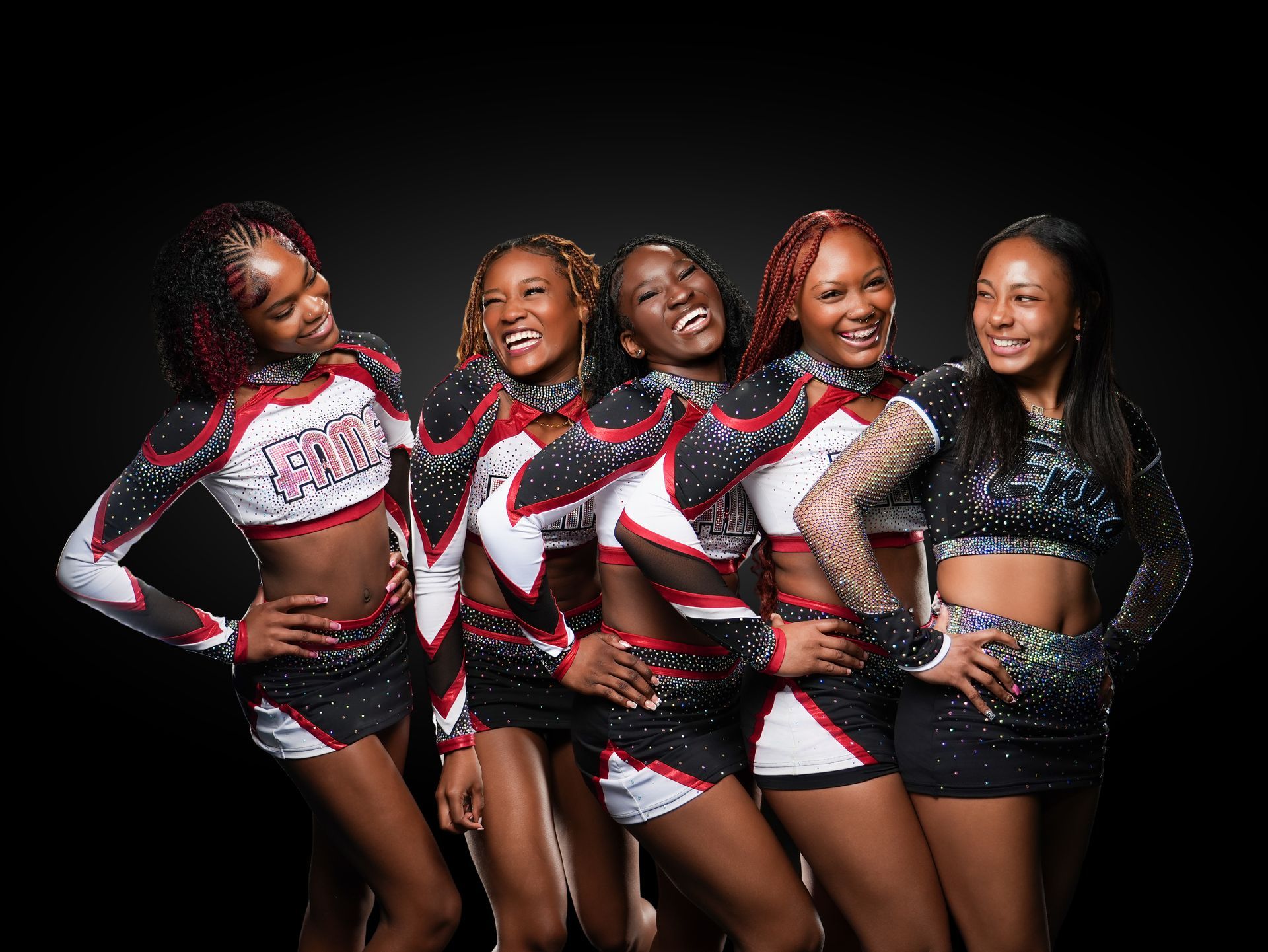 Five cheerleaders in red, black, and white uniforms posing against a black background