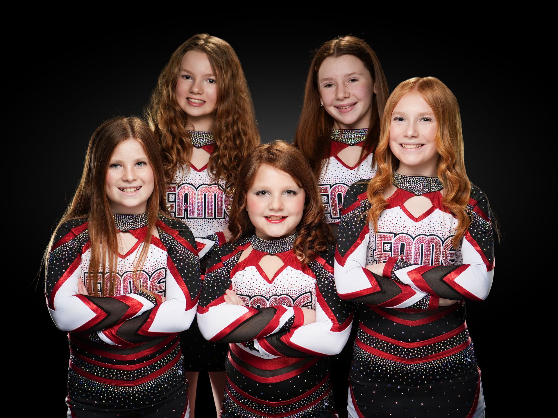 Five cheerleaders in red, black, and white uniforms posing against a black background