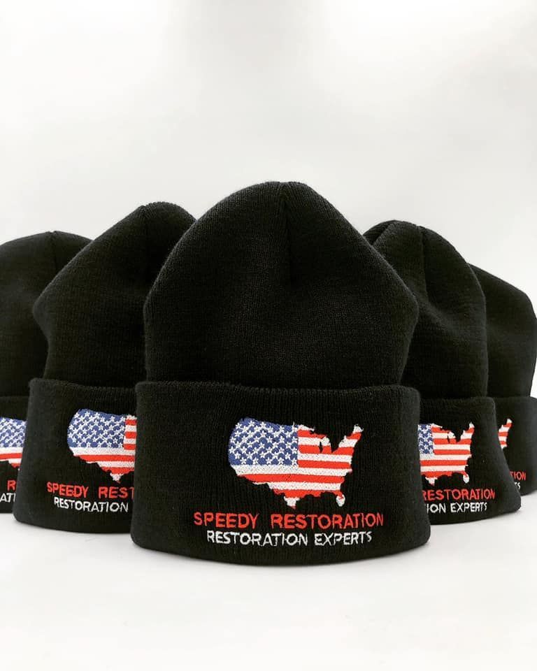 A bunch of black beanies with the words speedy restoration embroidered on them