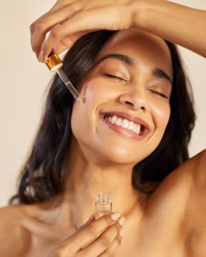 Una donna sorridente si applica un contagocce di siero per la cura della pelle sulla guancia.