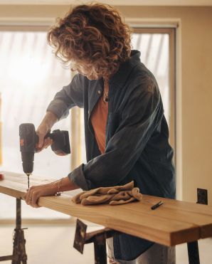 Persona che utilizza un trapano elettrico per installare una mensola di legno in casa.