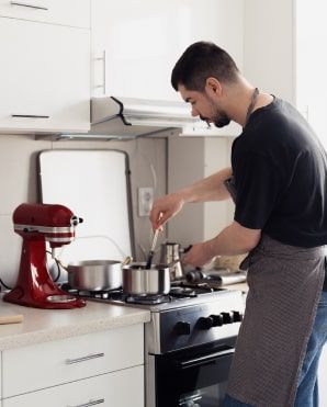 Un uomo cucina sui fornelli accanto a una planetaria rossa in una cucina bianca.