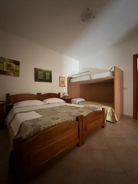 Camera da letto con due letti in legno, lenzuola bianche, quadri alle pareti e un letto a castello in un angolo.