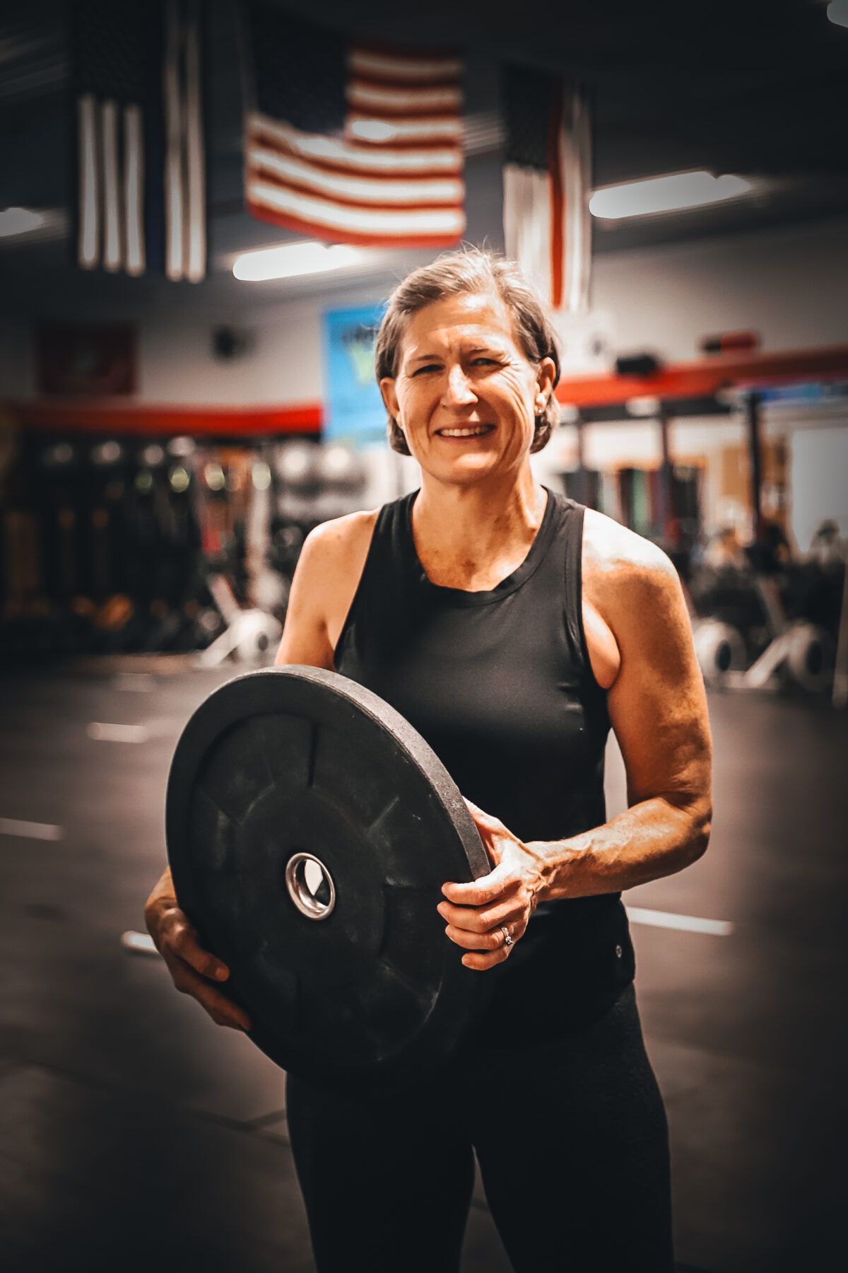 A woman is holding a barbell in a gym.