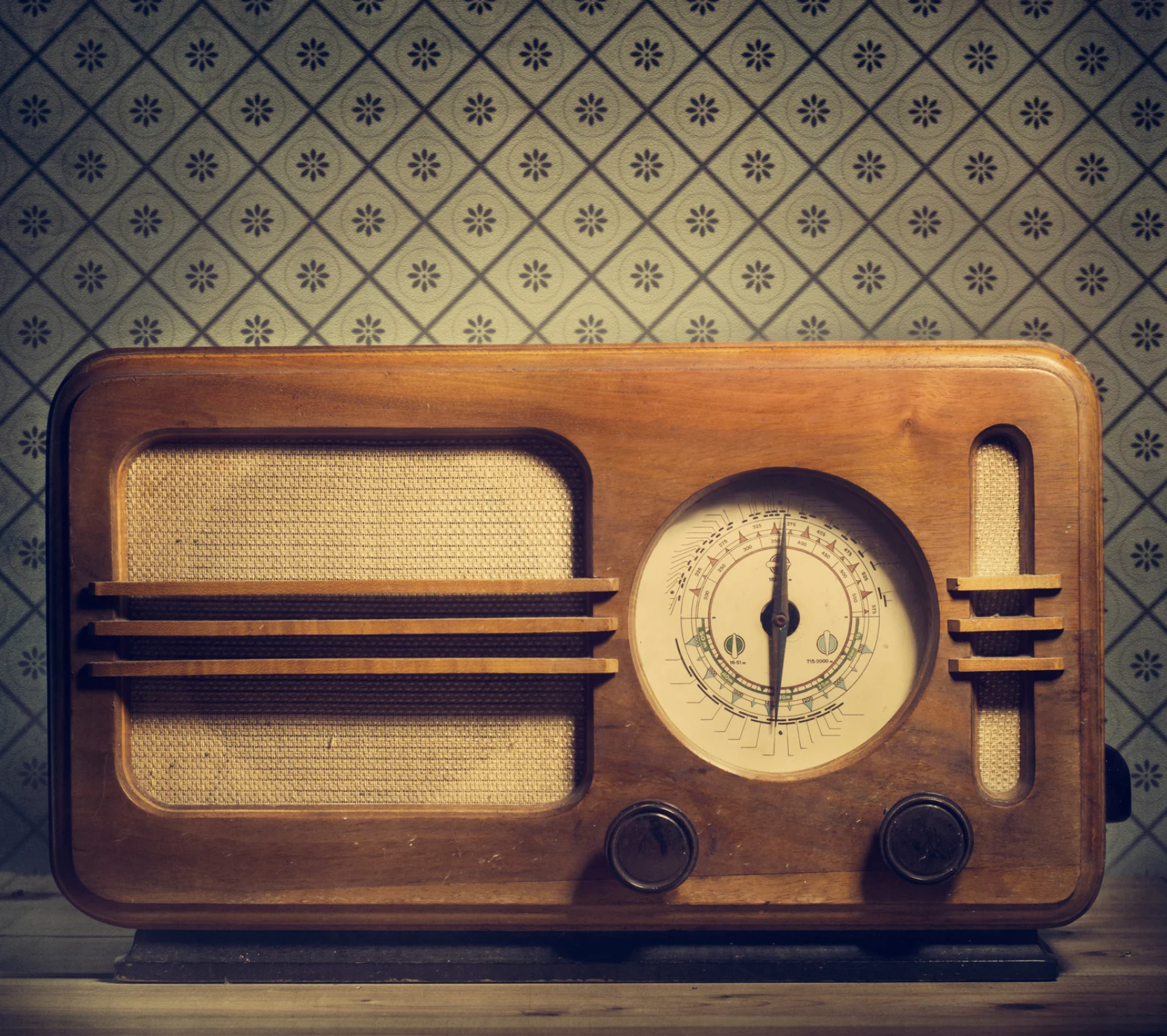 An old radio is sitting on a table in front of a patterned wallpaper