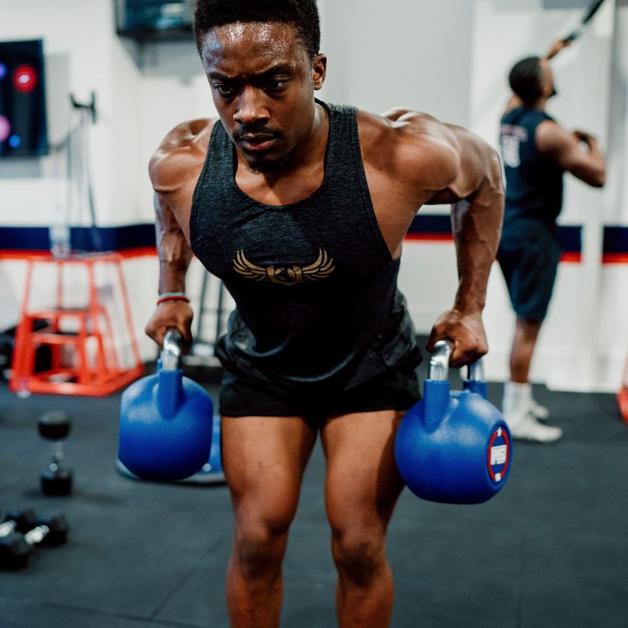 Athlete doing a bent-over kettlebell row in a gym, with a focused expression.