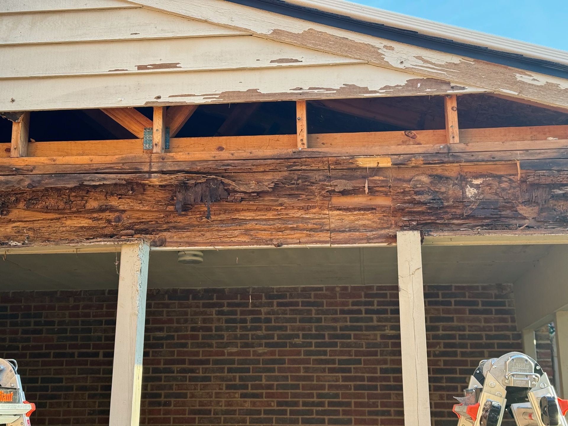 Damaged roof edge with peeling paint and exposed wood above a brick building.
