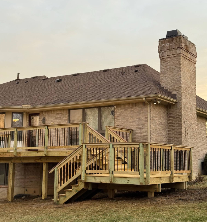 Newly built wooden deck on the back of a brick house with a chimney; overcast sky.