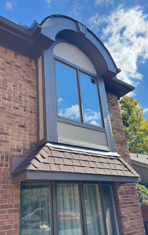 Brick building with large arched window framed in brown, blue sky reflection.