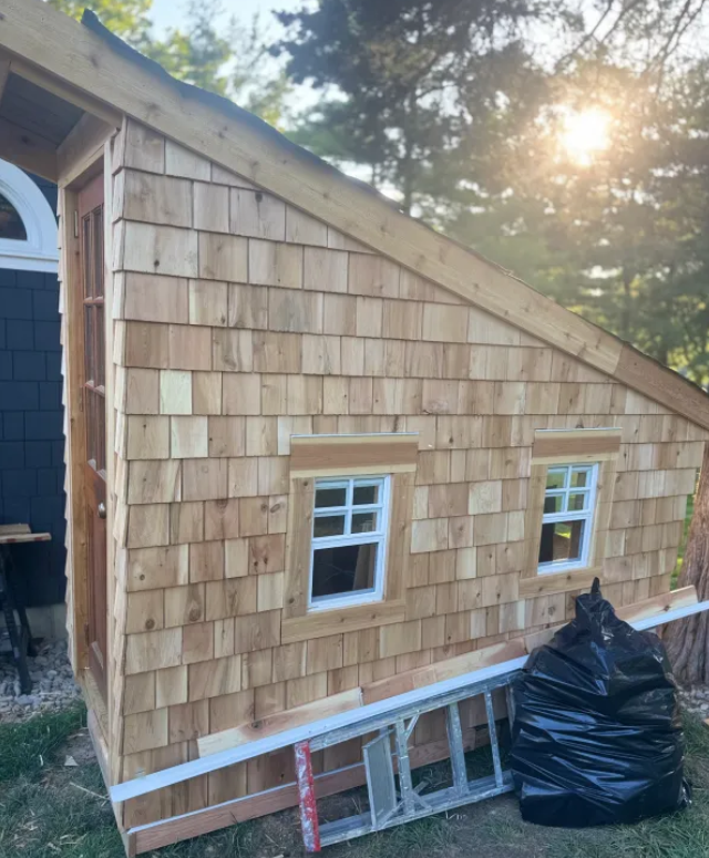 Wooden shed with cedar shake siding, two small windows, and a doorway.