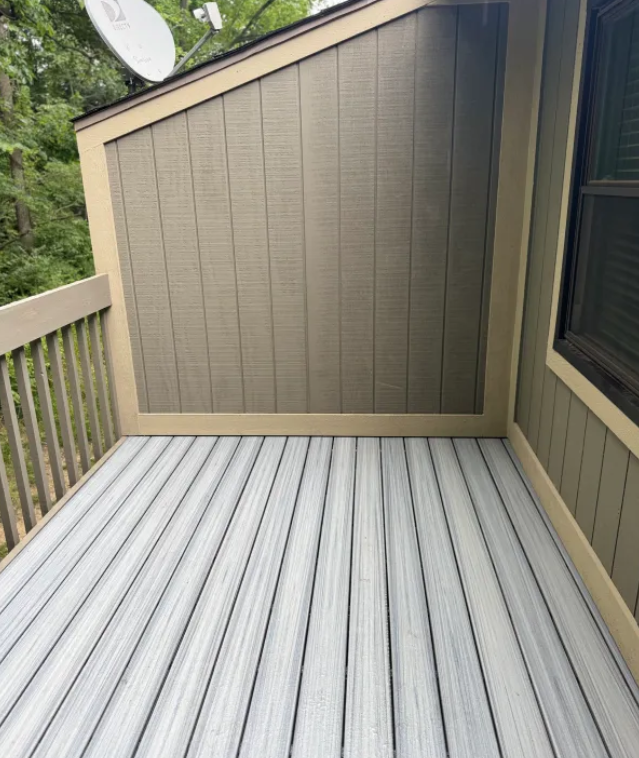 Empty outdoor deck with light gray composite flooring and tan siding, surrounded by a light brown trim.