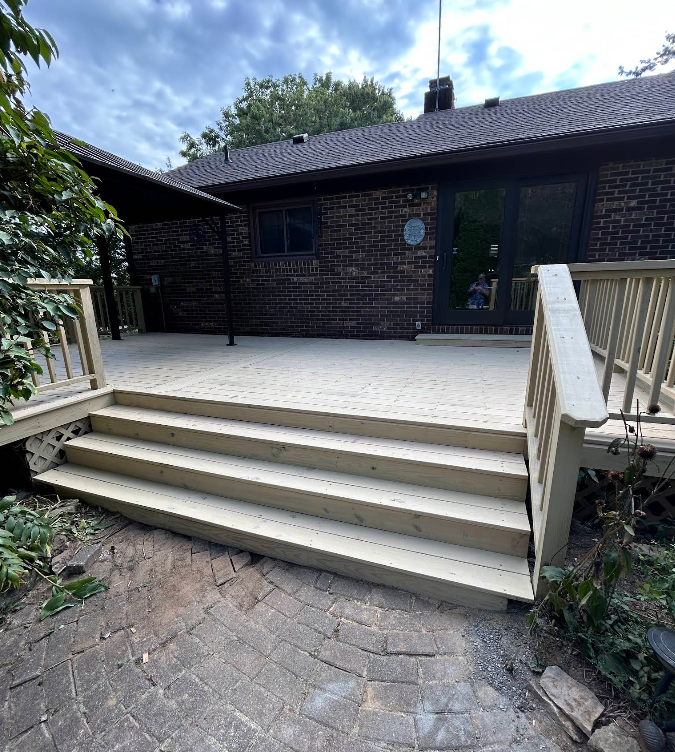 Wooden deck with steps leading down to a brick patio, against a brick house.