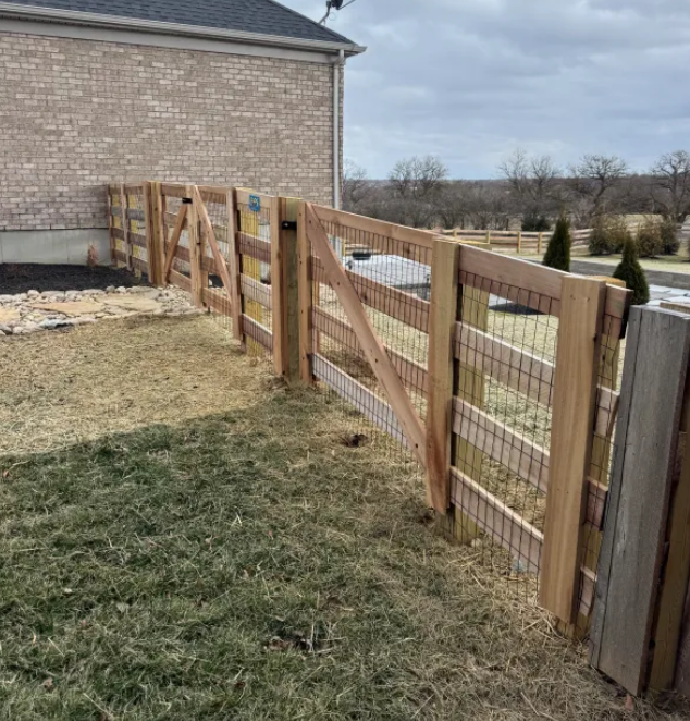 Wooden fence with wire mesh in a yard next to a brick building.