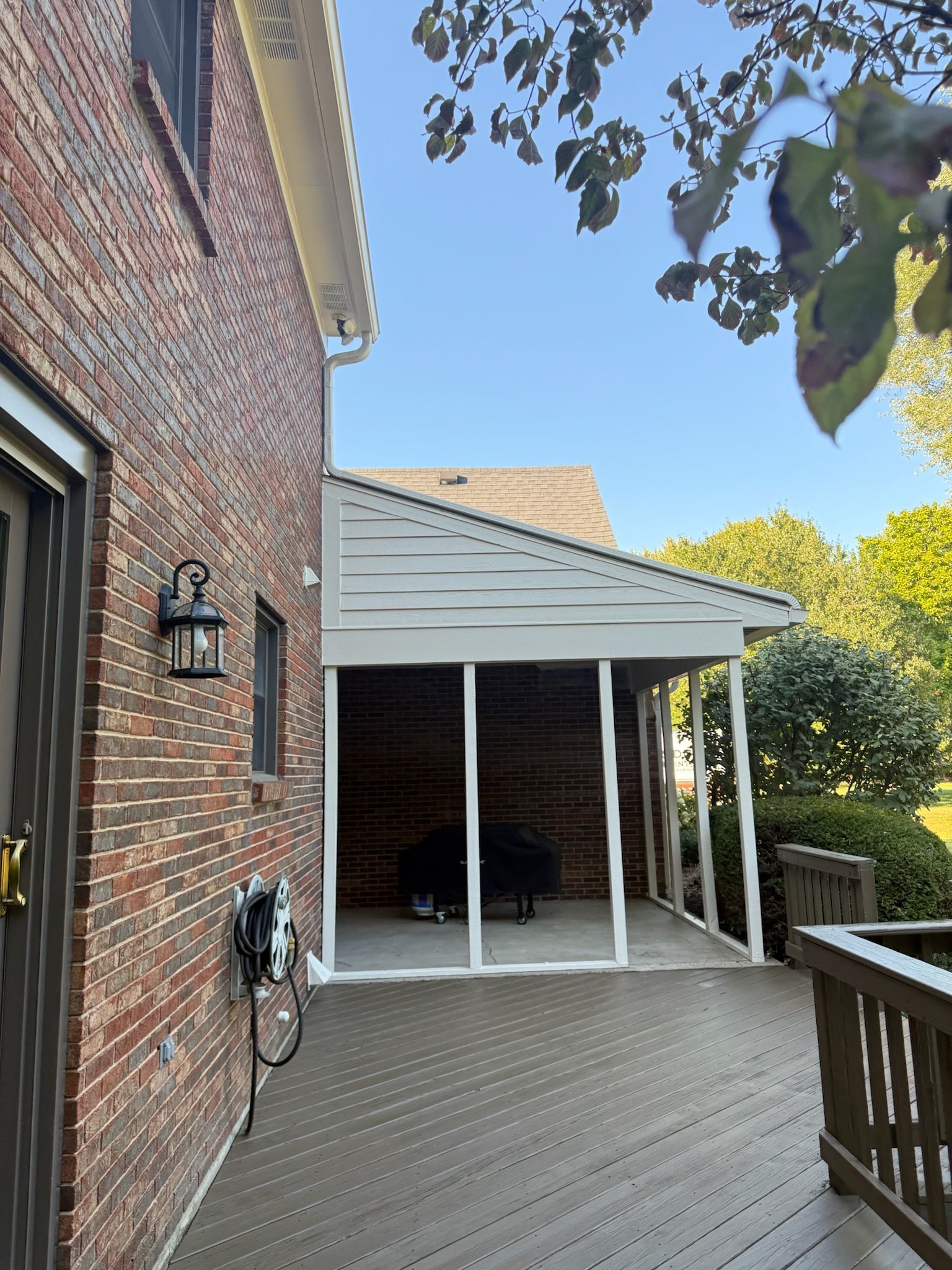 Brick house with screened porch and wooden deck. White trim, blue sky.