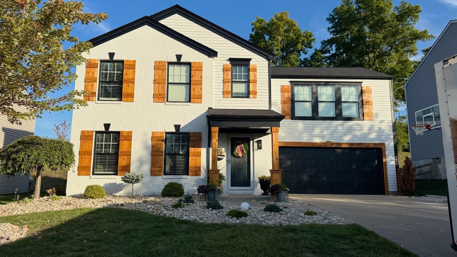 White two-story house with black trim, wooden shutters, and a black garage door.