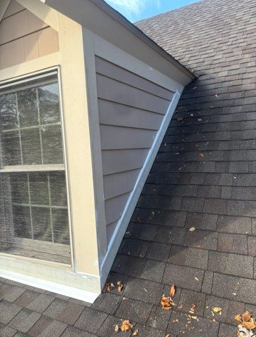 Triangular dormer with beige siding, window, and brown roof shingles.