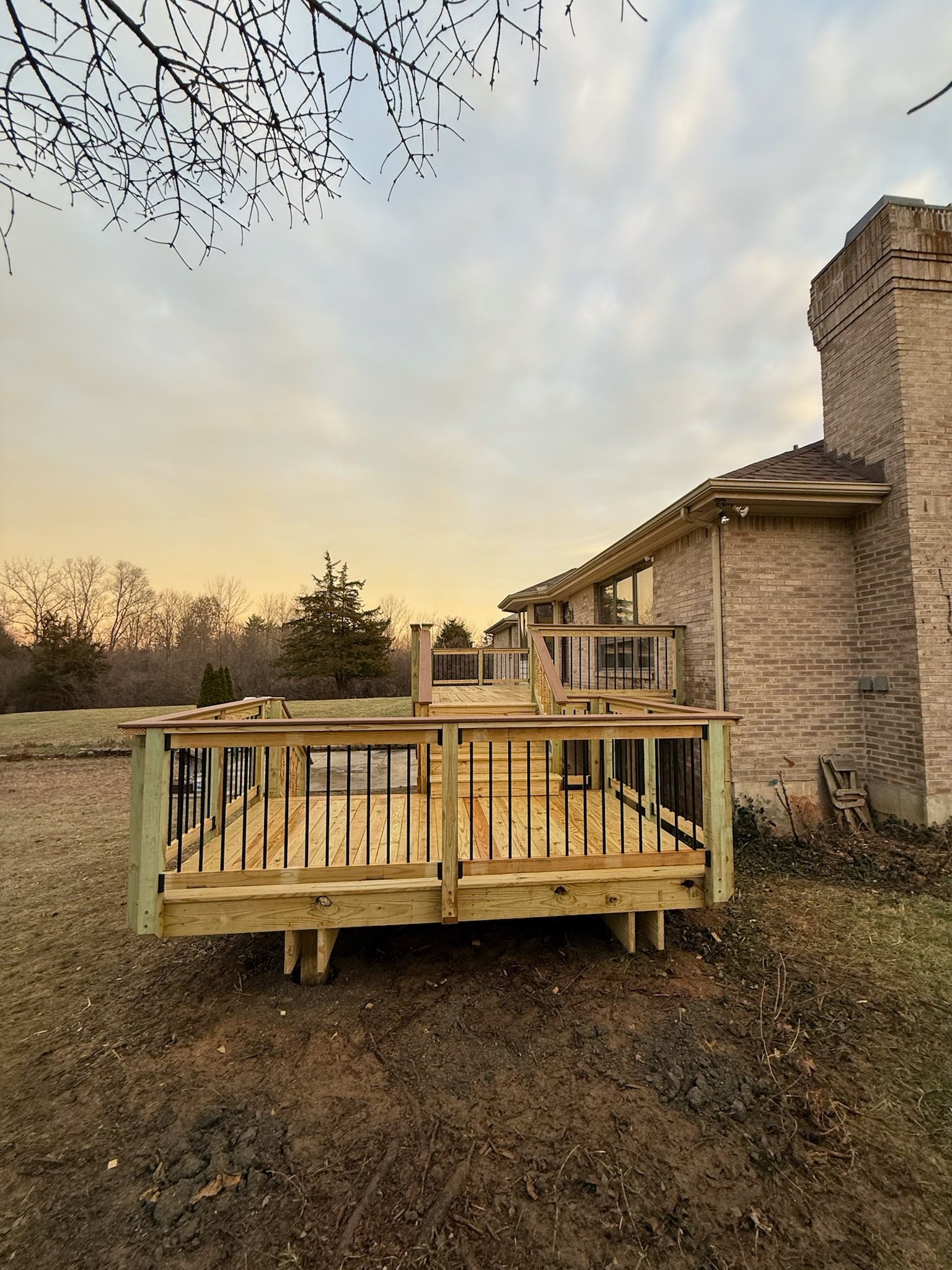 Newly built wooden deck with black railings next to a brick building under a cloudy sky.