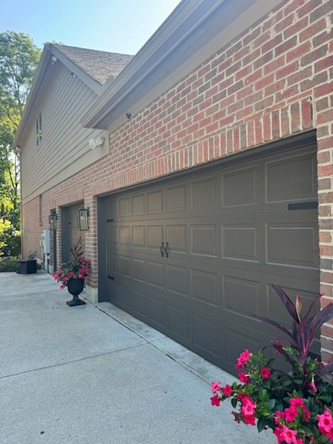 Brown garage doors on brick and siding building; planters with pink flowers.