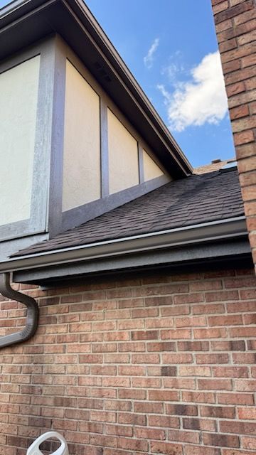 Brick building exterior with brown roof, gutters, and trim against a cloudy sky.