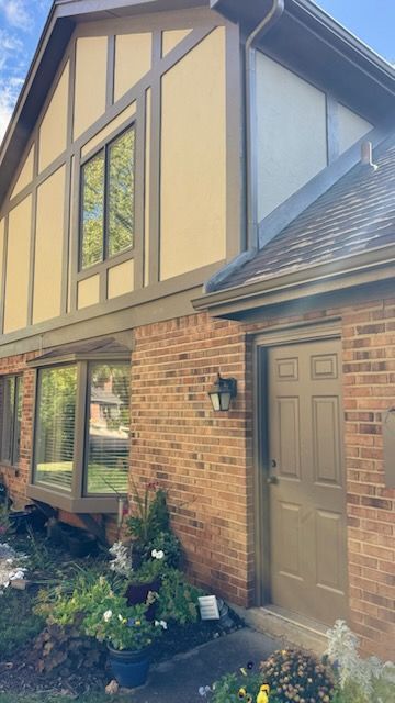Two-story brick house with brown trim and door. Large windows, landscaping in front.