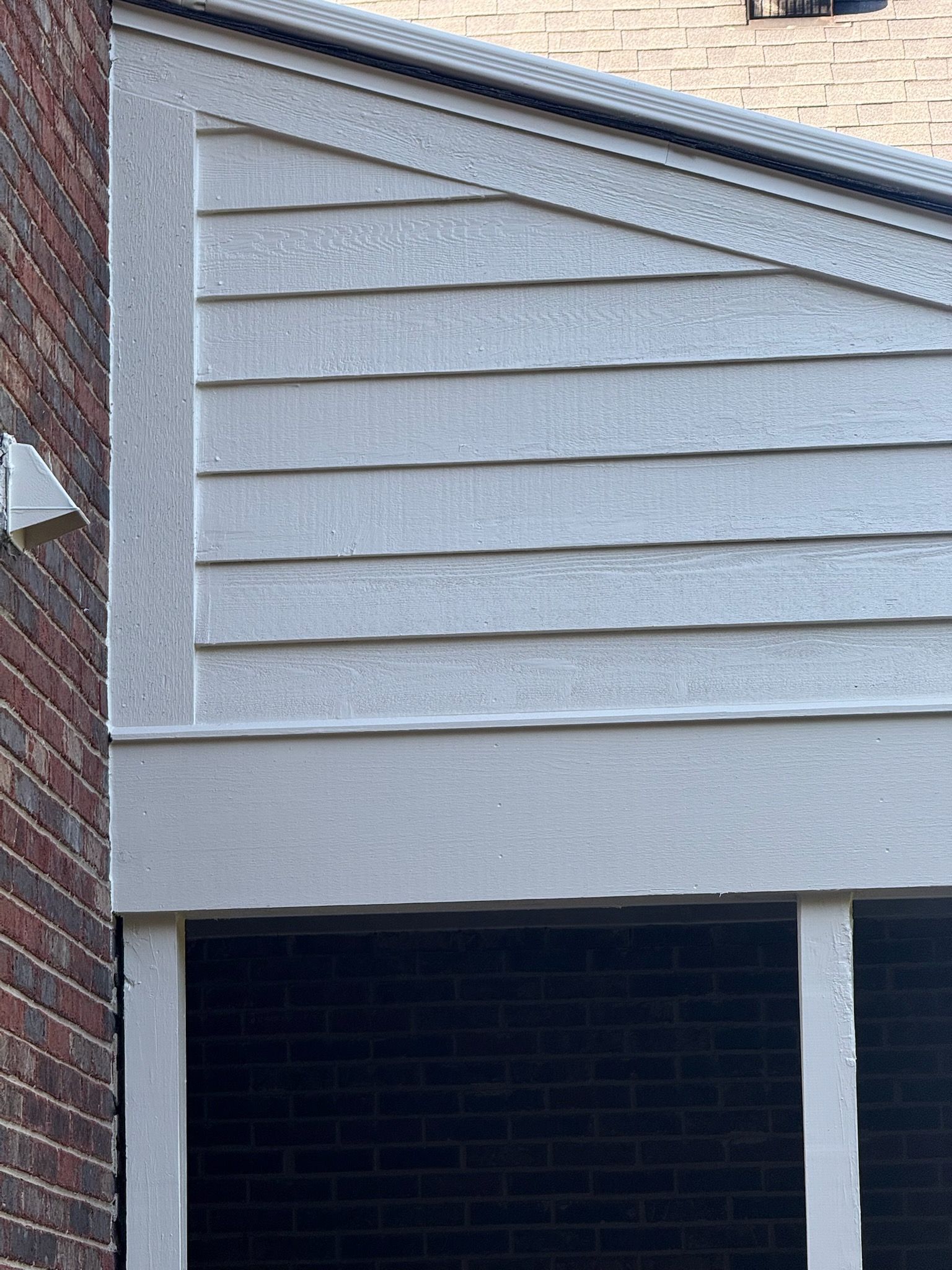 Gray siding with horizontal planks and angled top, bordering a porch area with brick.