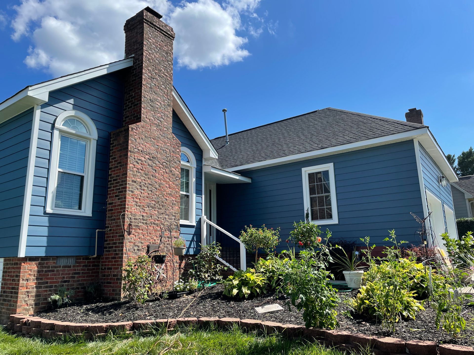 A blue house with a brick chimney is sitting on top of a lush green hillside.