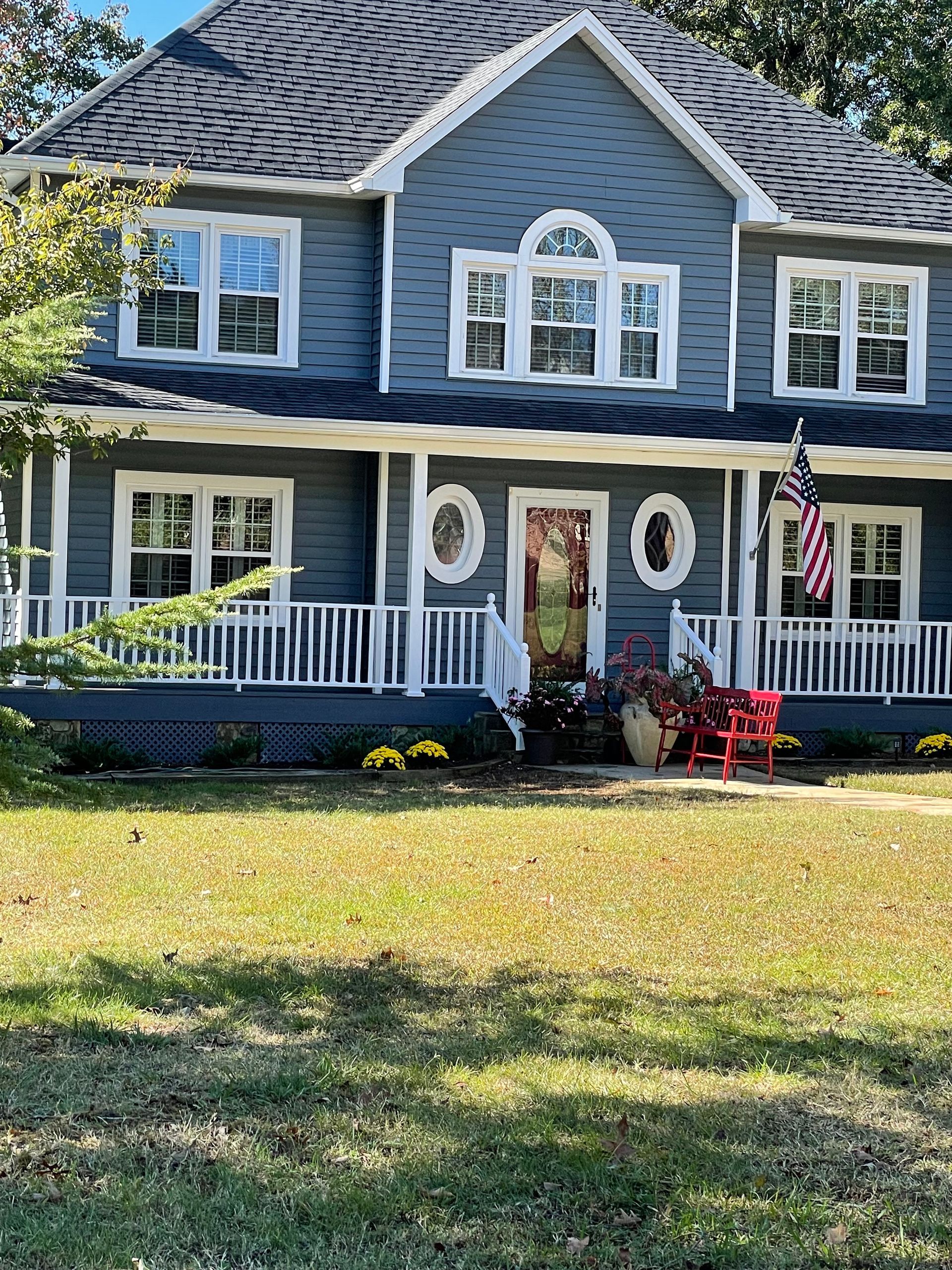 A large blue house with a large porch and a red chair in front of it.
