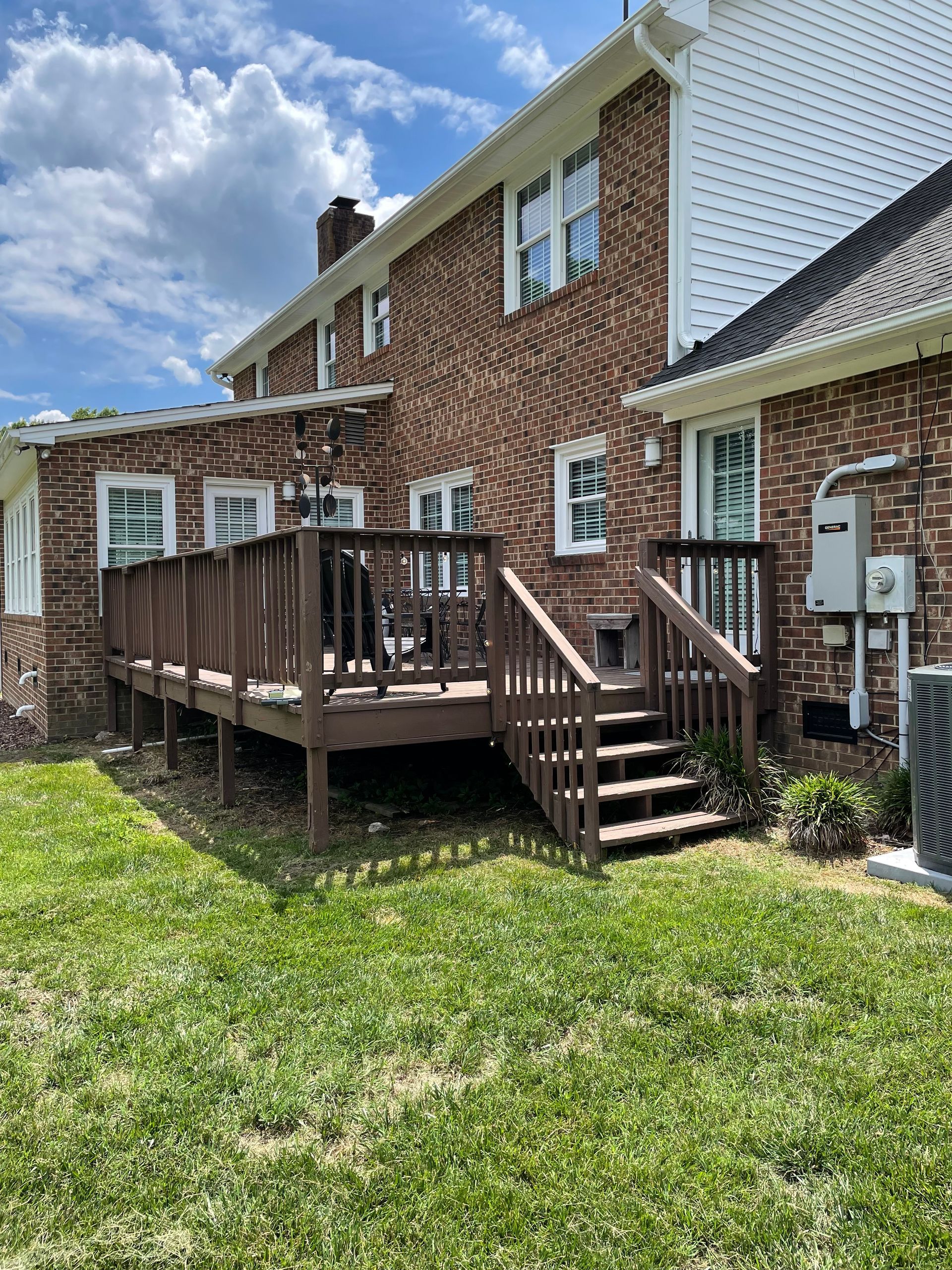 A brick house with a wooden deck and stairs in the backyard.