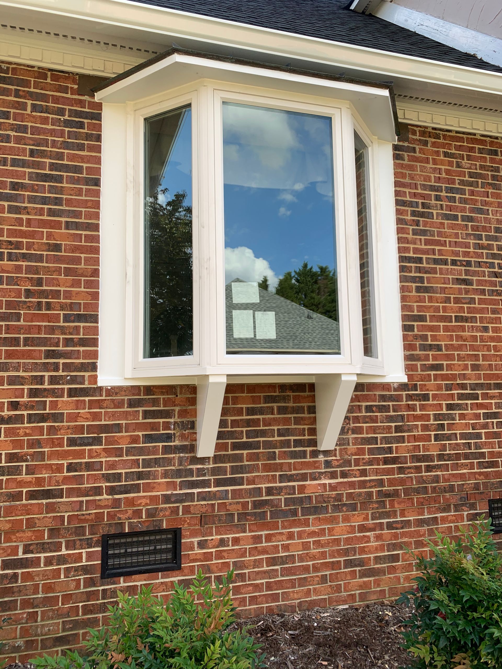 A white bay window is on the side of a brick house.