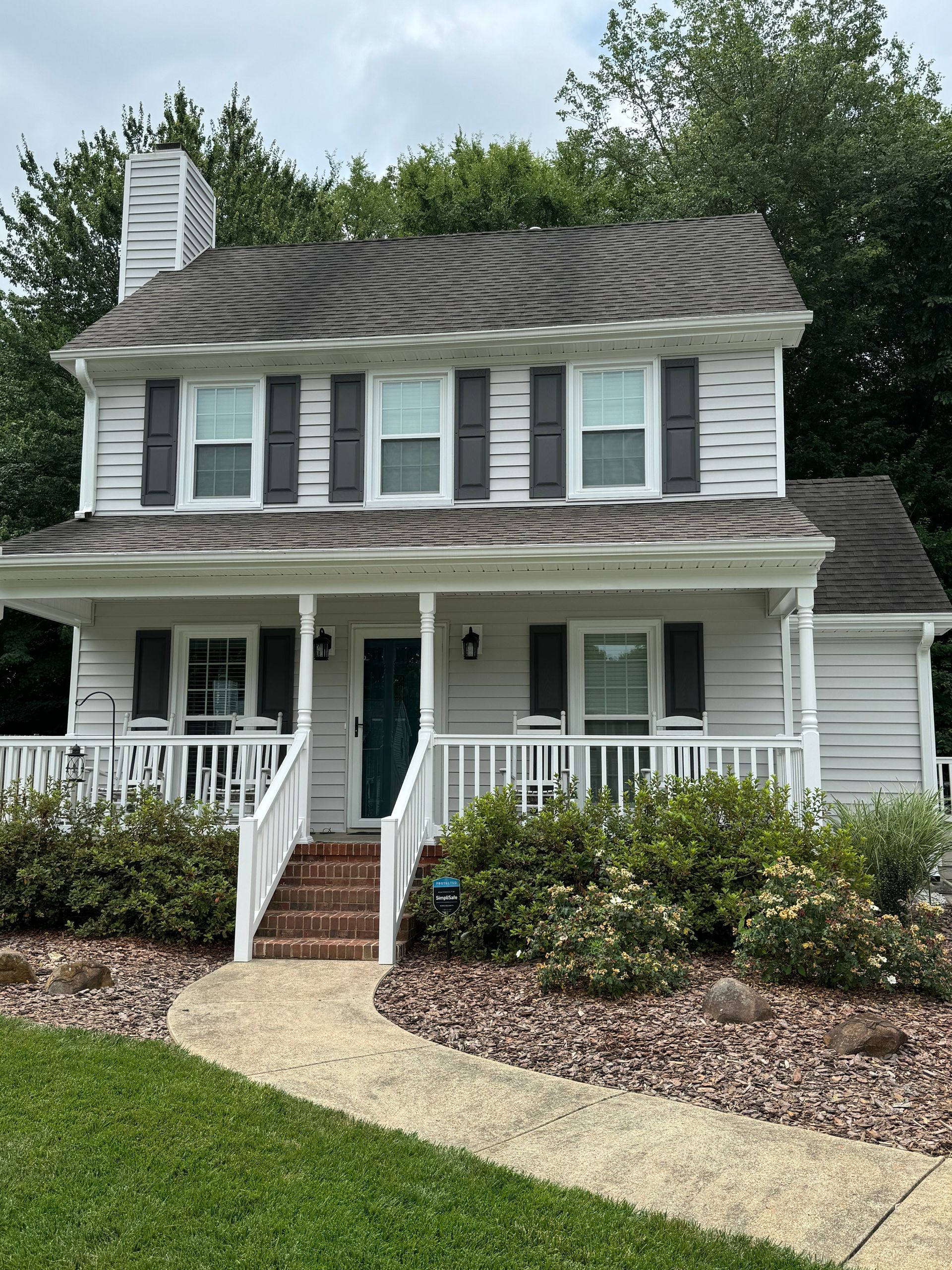 A white house with black shutters and a walkway leading to it.