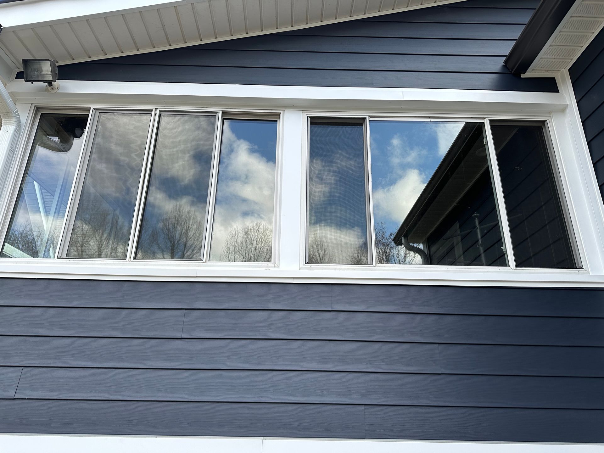 A large window on the side of a house with a blue siding and white trim.