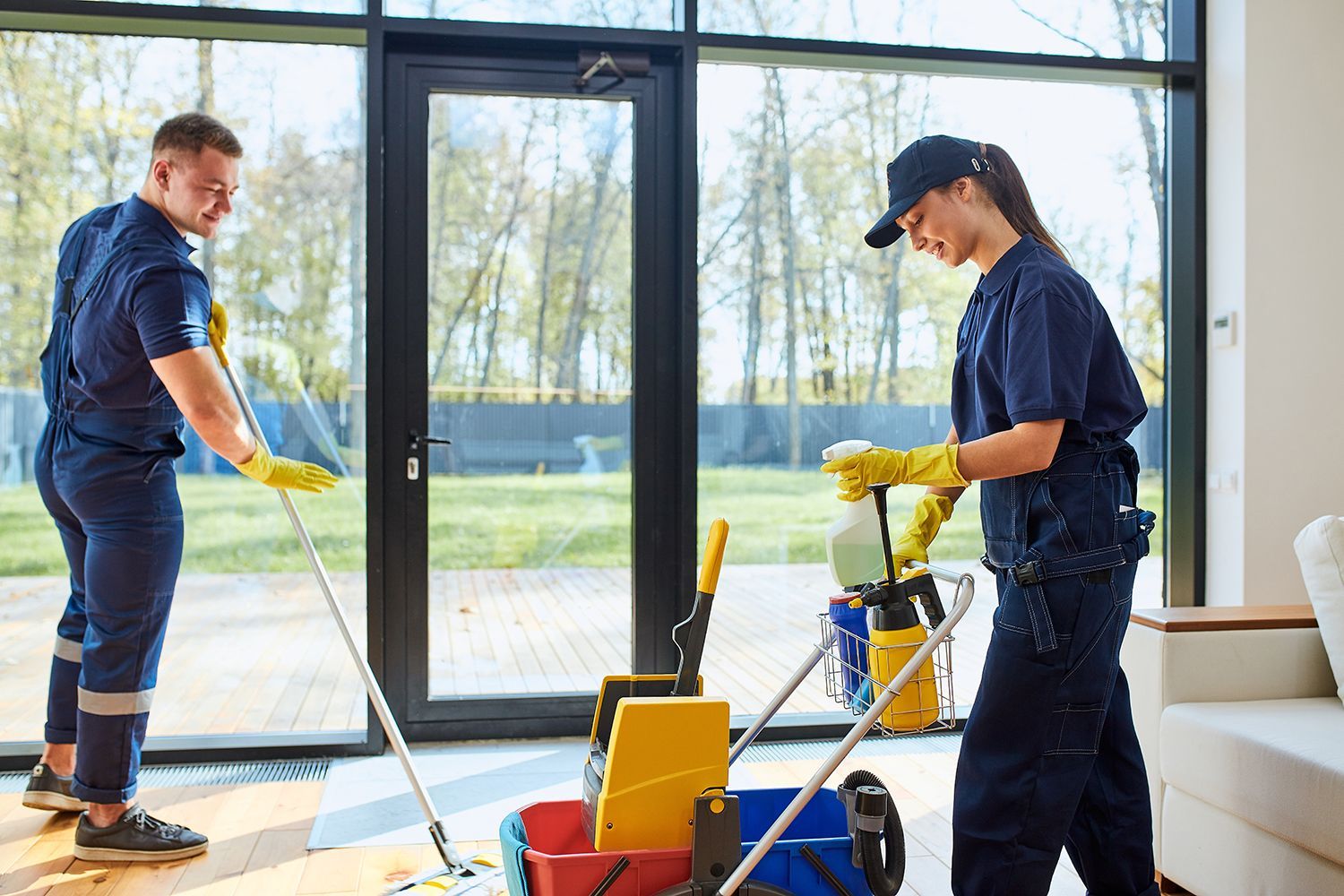 Two cleaners with equipment in a bright room by large windows Two cleaners with equipment in a bright room by large windows