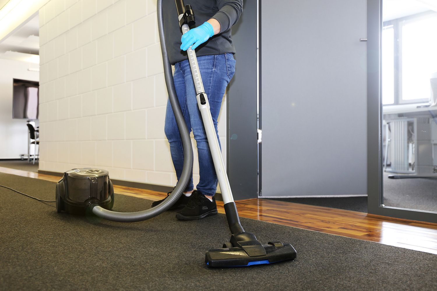 Worker vacuuming carpet in a hallway with a large upright cleaner and hose attachment Worker vacuuming carpet in a hallway with a large upright cleaner and hose attachment
