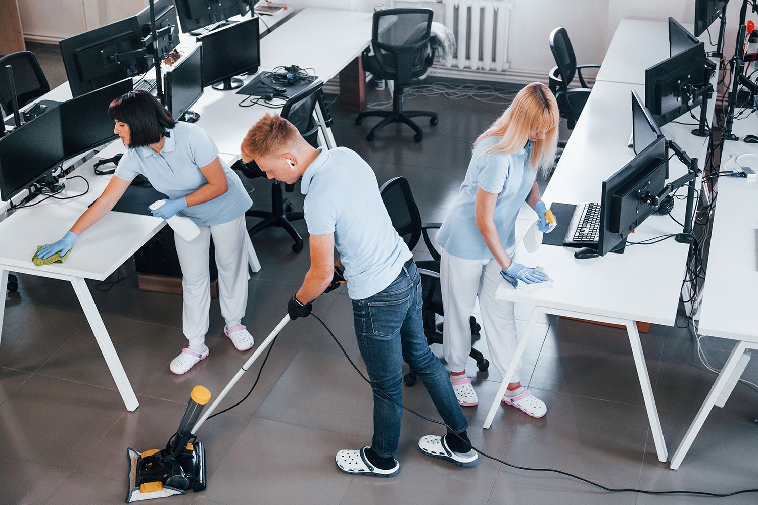 People cleaning an office with vacuum and mops around desks and computers People cleaning an office with vacuum and mops around desks and computers