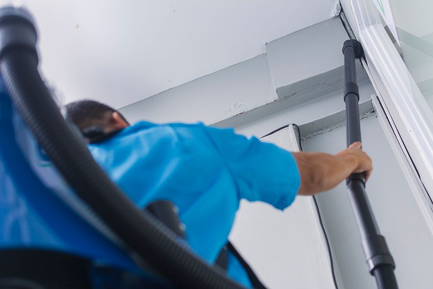 Worker in blue shirt cleaning air vents with a long vacuum in a ceiling corner Worker in blue shirt cleaning air vents with a long vacuum in a ceiling corner