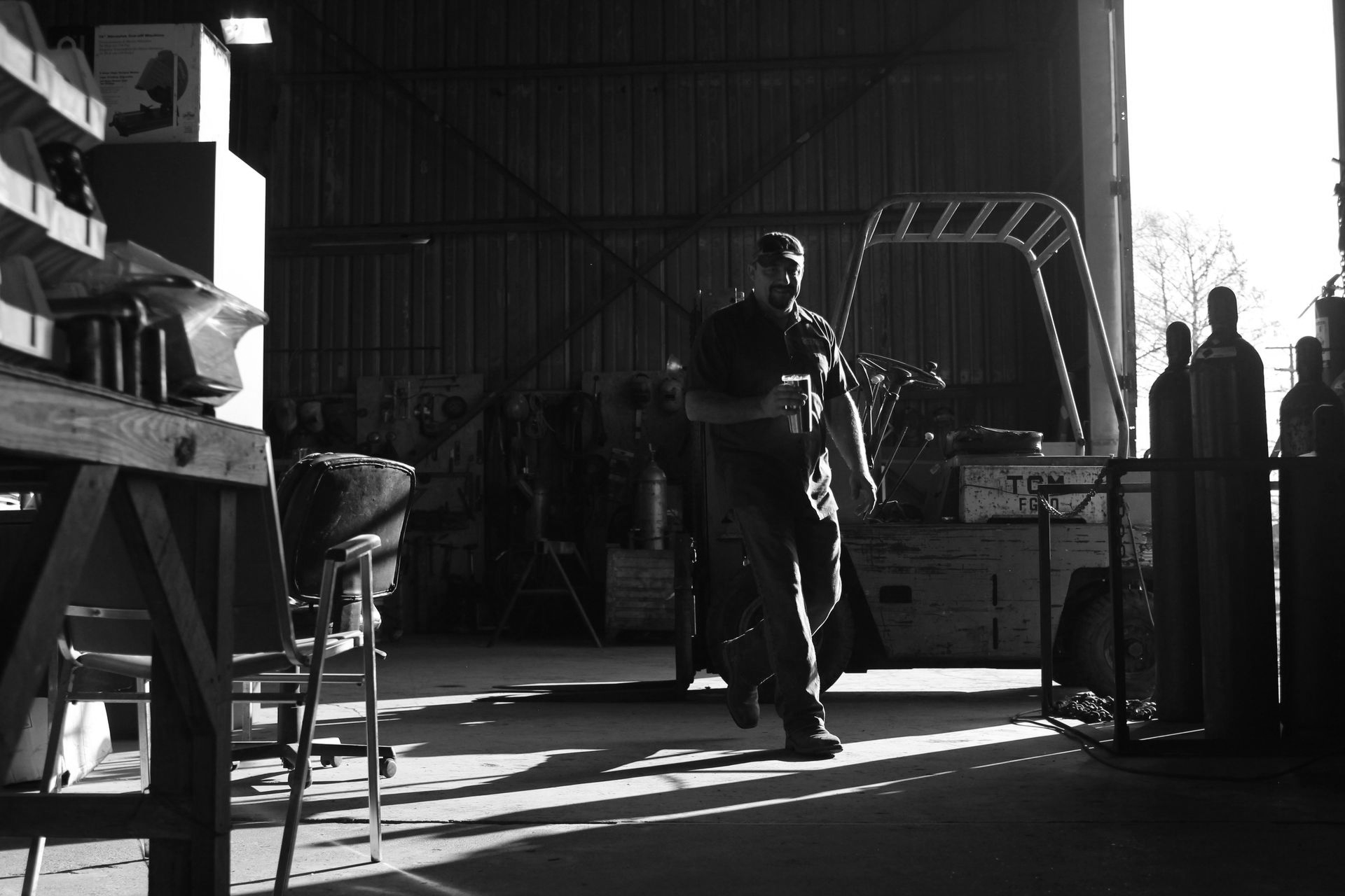 A person walking in a dimly lit workshop, bright sunlight from a large door illuminates the scene.