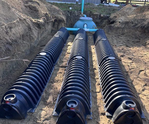 Three black corrugated drainage pipes laid in a trench, leading to a blue utility chamber under construction