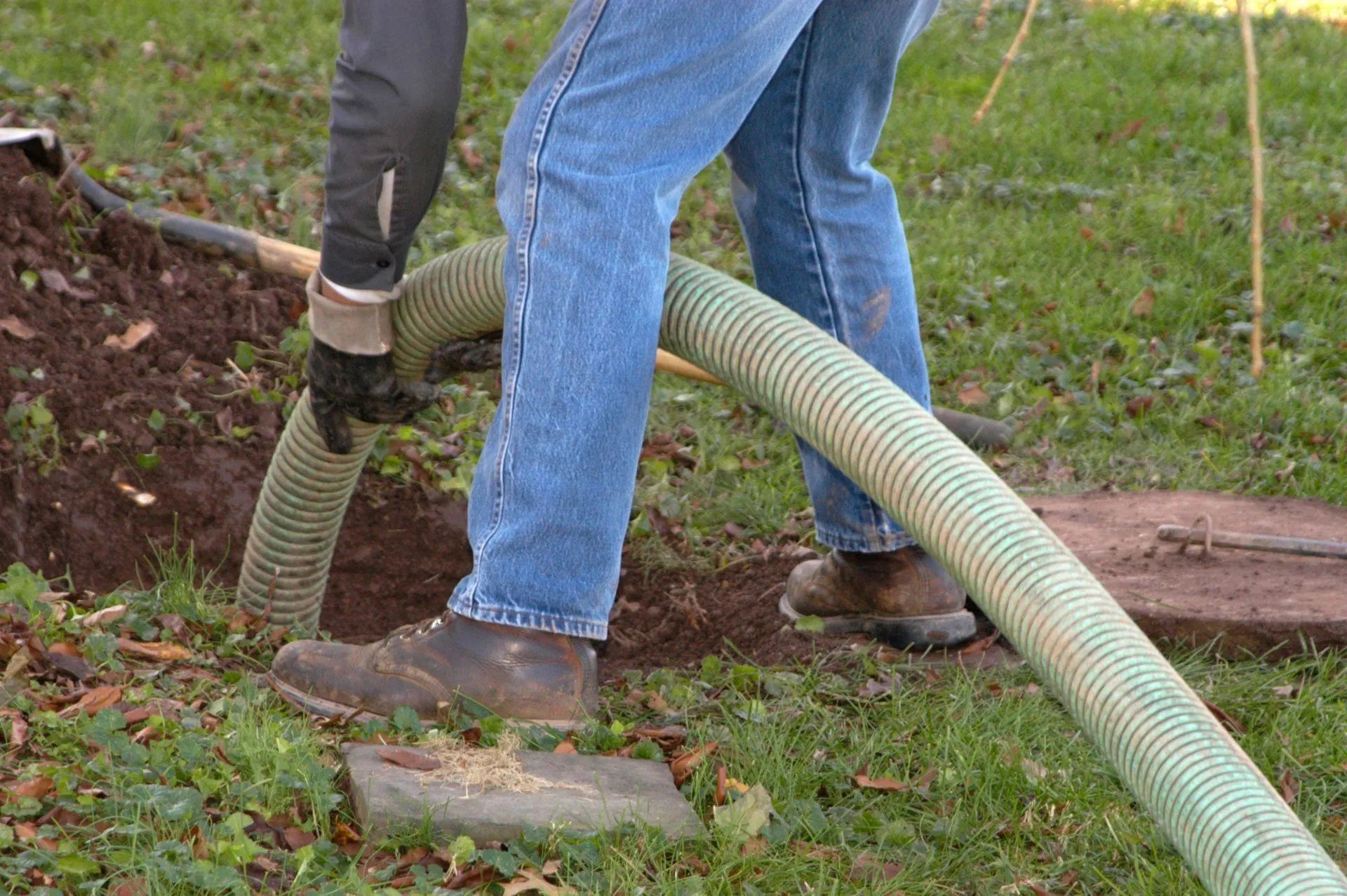 Two workers use a corrugated hose to suction soil around a garden bed.