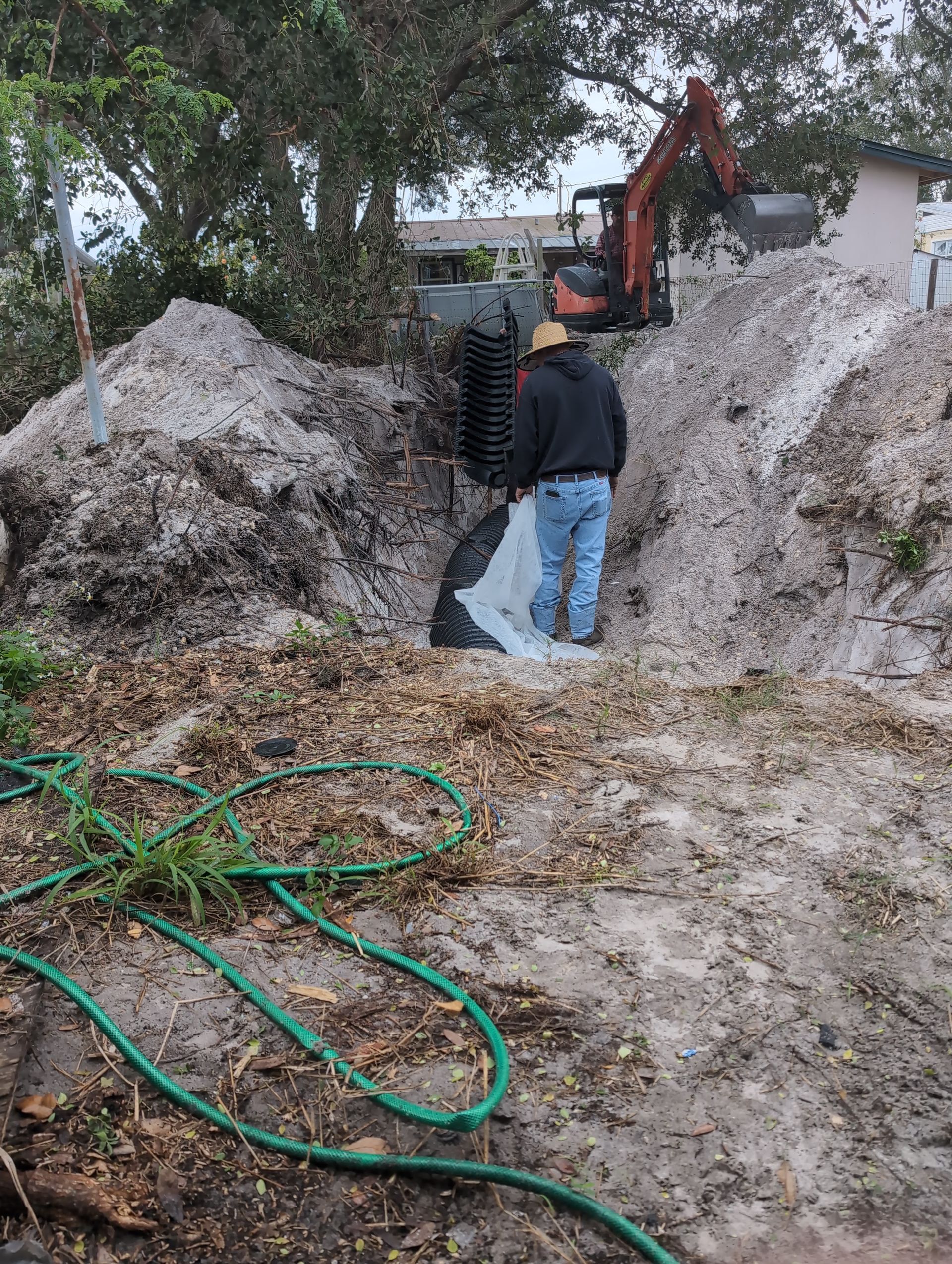 Worker using an orange excavator among dirt mounds and hose in a muddy yard