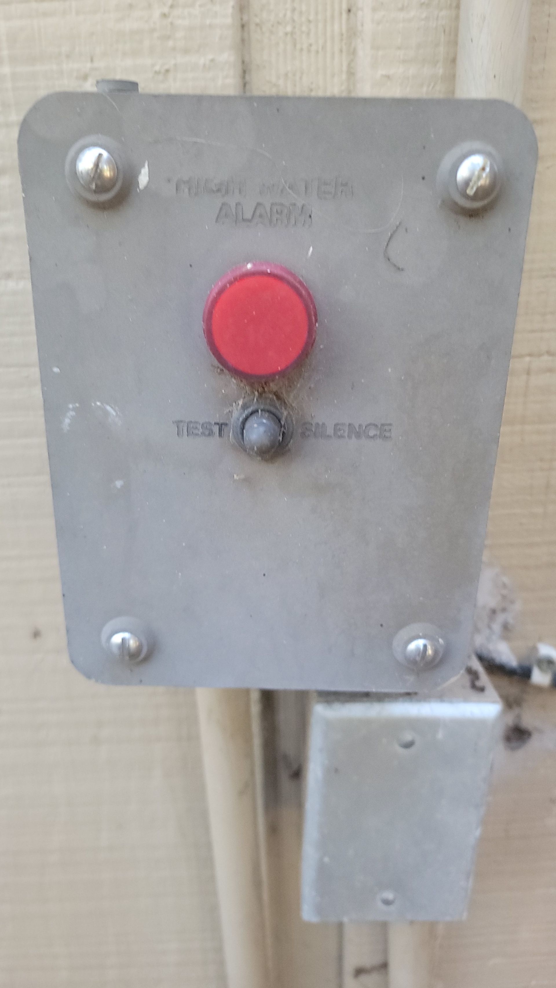 Metal emergency stop button panel with a red push button and smaller switch below on a wall