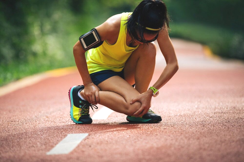 Runner Clutching Her Ankle on a Red Track — Goulburn Physiotherapy Centre in Goulburn, NSW