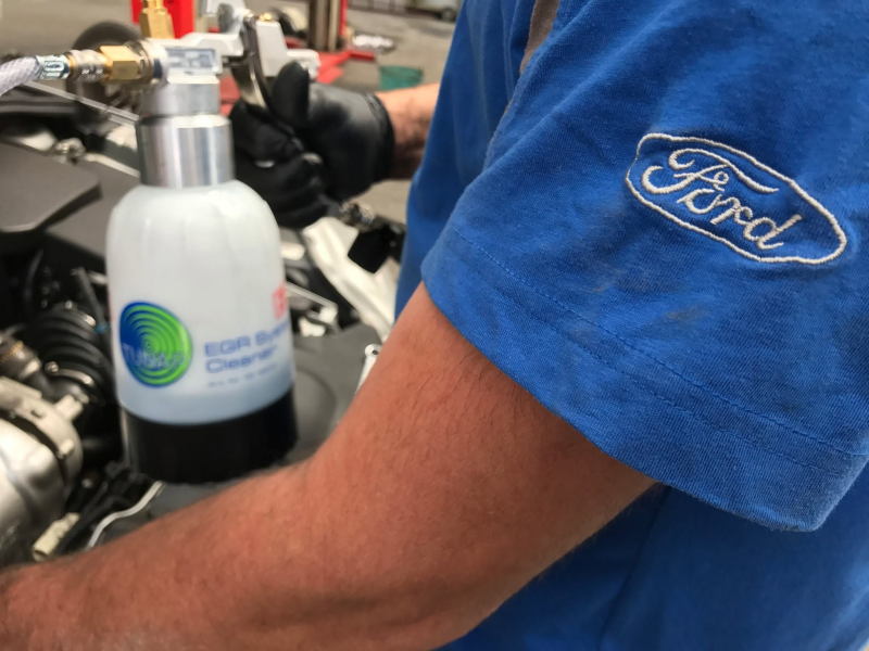 Logo Ford su una camicia blu accanto a una bottiglia attaccata al manubrio di una motocicletta.