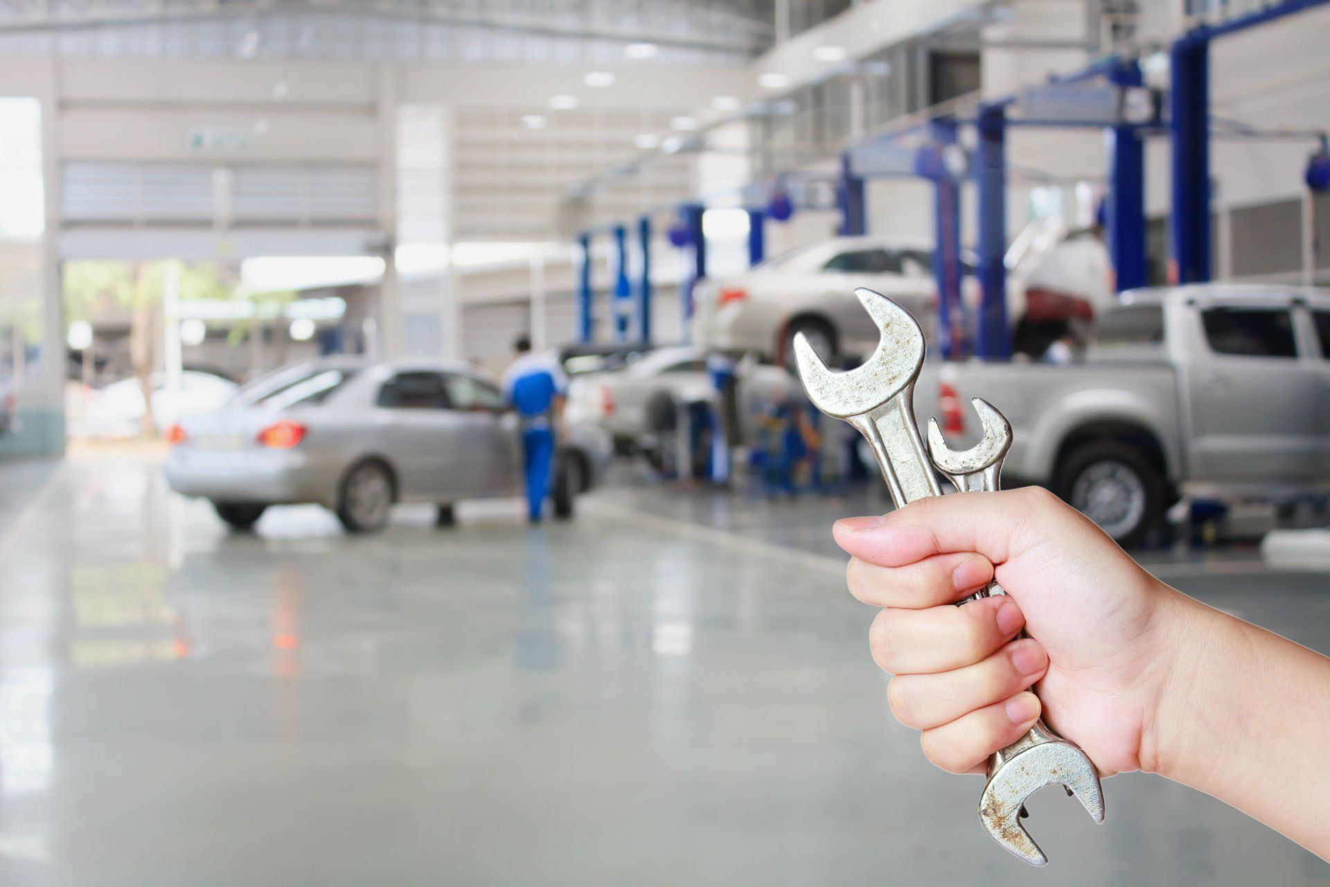 Una mano che impugna una chiave inglese in un'officina meccanica, con auto e meccanici sullo sfondo.