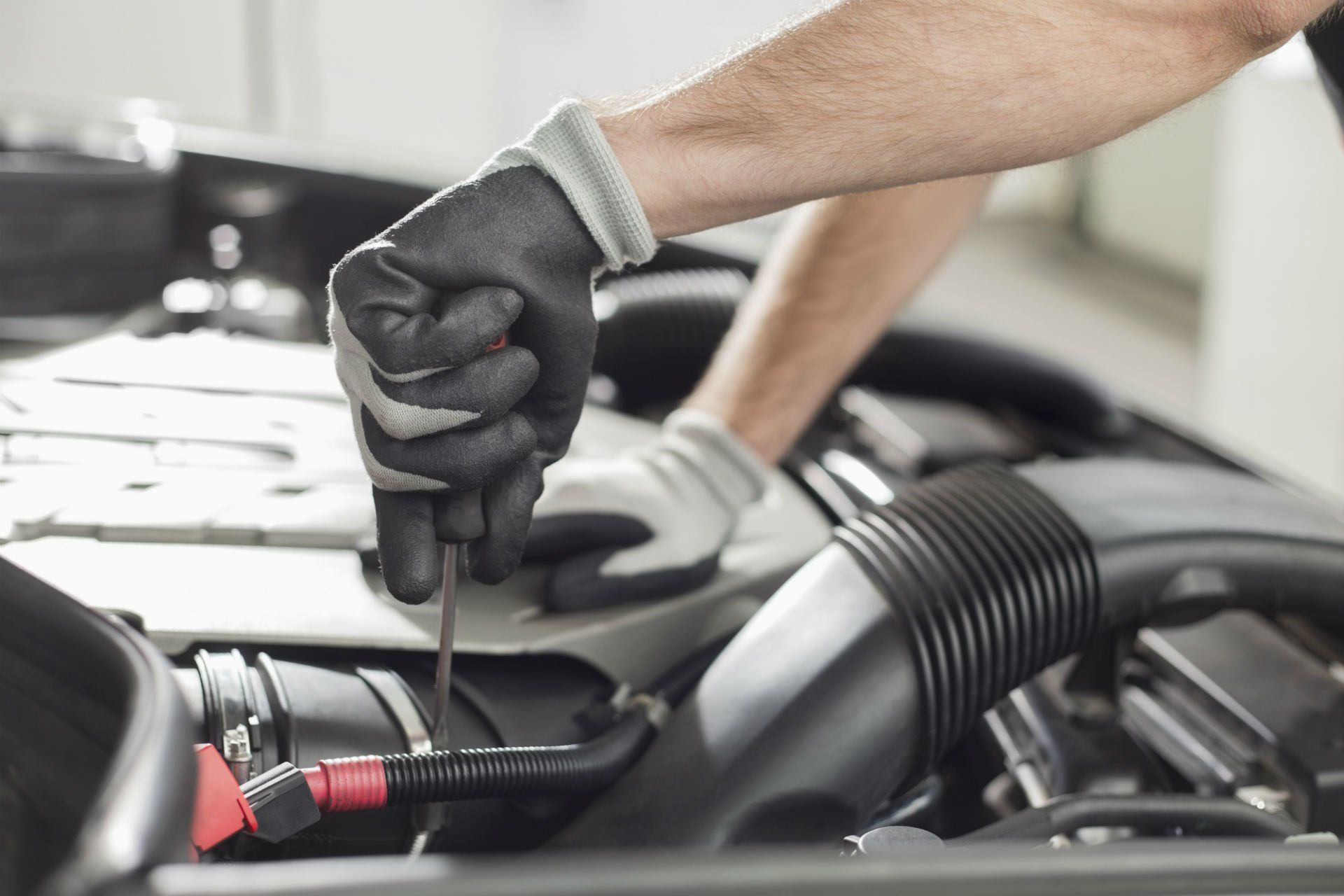 Mano guantata che controlla l'olio motore nel vano motore di un'auto con l'astina di livello
