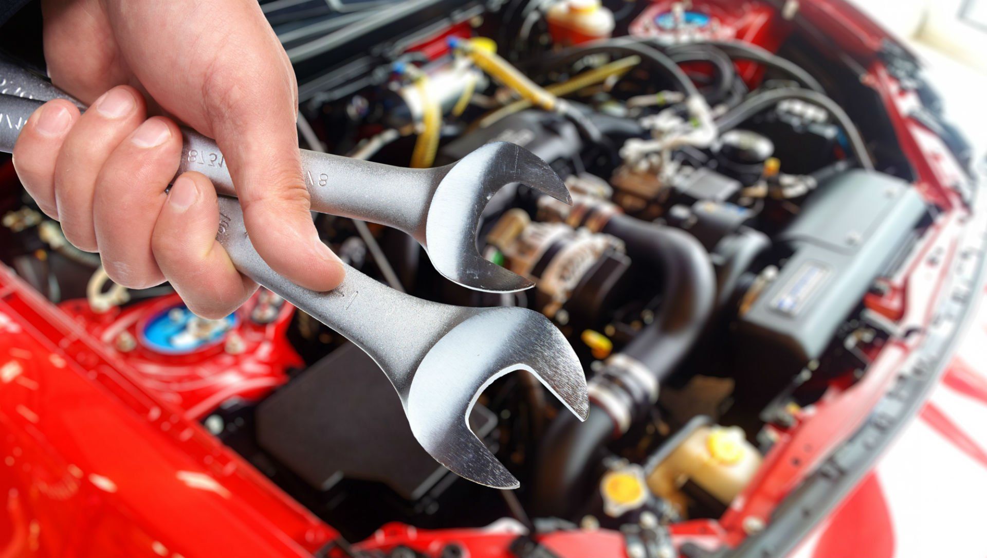 Una mano che impugna una chiave inglese sopra il motore di un'auto rossa in un garage.