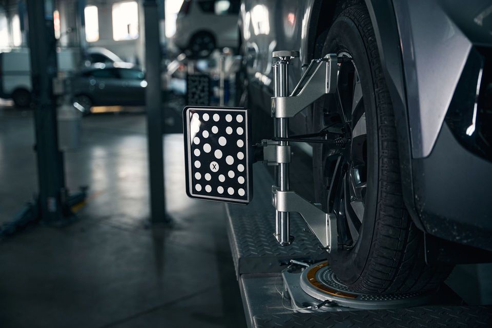Attrezzatura per l'allineamento delle ruote fissata alla ruota anteriore di un'auto in un'officina, con un pannello di riferimento in bianco e nero.